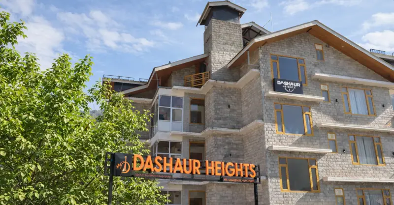 Stone façade of Dashaur Heights hotel with its illuminated signboard in Burwa, Manali